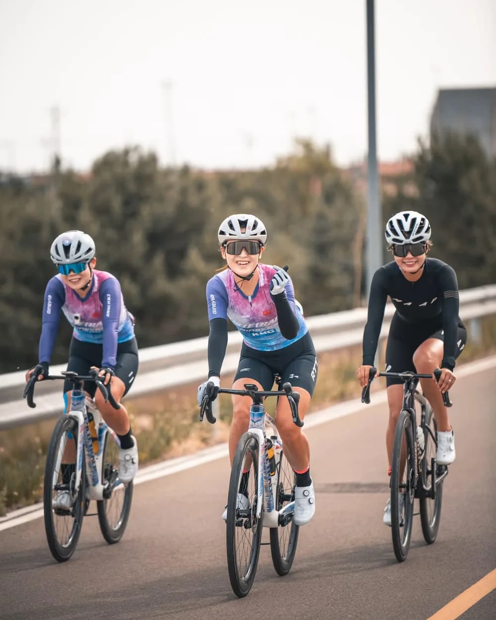Três ciclistas sorrindo durante o pedal, em uma pista ao ar livre