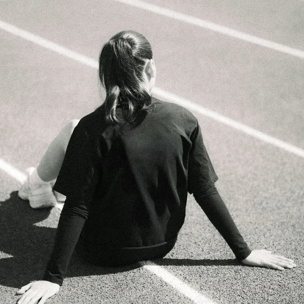Atleta de costas, sentada na pista de corrida, em preto e branco